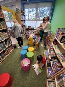 Na zdjęciu znajdują się uczestnicy warsztatów. Dzieci siedzą na poduszkach pomiędzy regałami. Zdjęcie wykonano w bibliotece.