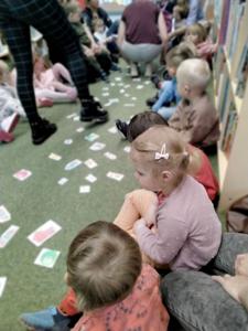 Na zdjęciu znajdują się uczestnicy warsztatów. Dzieci siedzą na poduszkach. Zdjęcie wykonano w bibliotece.