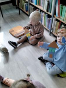 Na zdjęciu znajdują się uczestnicy warsztatów. Dzieci siedzą na poduszkach i wykonują prace plastyczne. Zdjęcie wykonano w bibliotece.