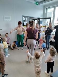Na zdjęciu znajdują się uczestnicy warsztatów. Dzieci stoją w kręgu i wykonują zadania. Zdjęcie wykonano w bibliotece.