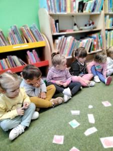 Na zdjęciu znajdują się uczestnicy warsztatów. Dzieci oglądają książki. Zdjęcie wykonano w bibliotece.
