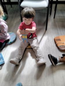 Na zdjęciu znajdują się uczestnicy warsztatów. Dzieci siedzą na poduszkach i wykonują prace plastyczne. Zdjęcie wykonano w bibliotece.