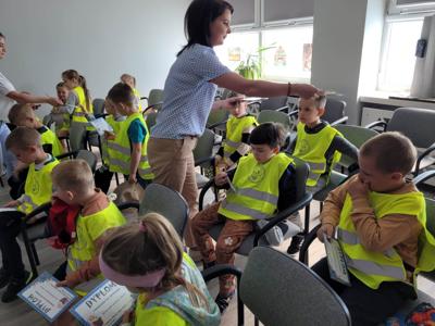 Na zdjęciu znajdują się uczestnicy zajęć. Dzieci siedzą na krzesłach. Zdjęcie wykonano w bibliotece.