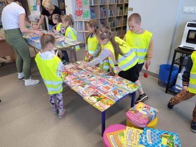 Na zdjęciu znajdują się uczestnicy zajęć. Dzieci oglądają książki. Zdjęcie wykonano w bibliotece.
