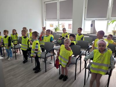 Na zdjęciu znajdują się uczestnicy zajęć. Dzieci siedzą i stoją. Zdjęcie wykonano w bibliotece.