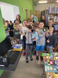 Na zdjęciu znajdują się uczestnicy kiermaszu. W tle księgozbiór biblioteki. Zdjęcie wykonano w bibliotece.