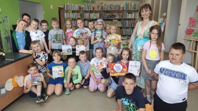 Na zdjęciu znajdują się uczestnicy kiermaszu. W tle księgozbiór biblioteki. Zdjęcie wykonano w bibliotece.
