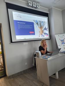 Na zdjęciu znajduje się Pani prowadząca warsztaty. W tle wyświetlana prezentacja multimedialna.