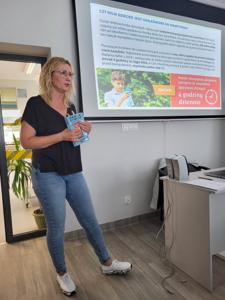 Na zdjęciu znajduje się Pani prowadząca warsztaty. W tle wyświetlana prezentacja multimedialna.