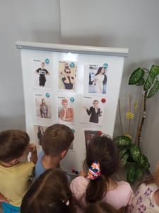 Na zdjęciu się uczestnicy zajęć. Dzieci patrzą na tablice z postaciami. Zdjęcie wykonano w bibliotece.
