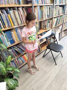 Na zdjęciu się uczestniczka zajęć. Dziewczynka trzyma w ręce kartkę. Zdjęcie wykonano w bibliotece.