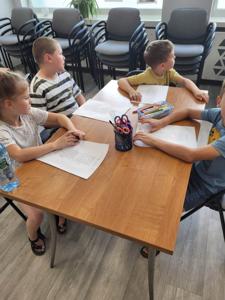 Na zdjęciu znajdują się uczestnicy zajęć. Dzieci wykonują prace plastyczne i powierzone im zadania.