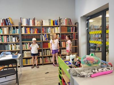 Na zdjęciu znajdują się uczestnicy zajęć. Uczestnicy wykonują zadania. W tle księgozbiór biblioteki.  Zdjęcie wykonano w bibliotece.