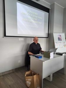 Na zdjęciu znajduje się prelegent. W tle wyświetlana prezentacja multimedialna. Zdjęcie wykonano w bibliotece.