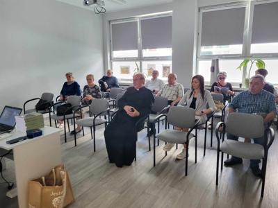 Na zdjęciu znajdują się uczestnicy spotkania. Uczestnicy siedzą na krzesłach. Zdjęcie wykonano w bibliotece.