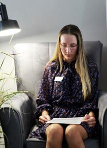 Na zdjęciu znajdują się uczestniczka czytająca książkę siedząc na fotelu. Zdjęcie wykonano w bibliotece.