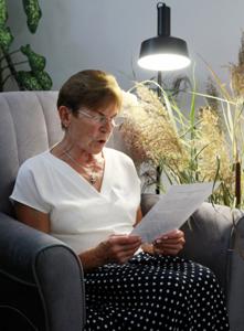 Na zdjęciu znajdują się uczestniczka czytająca książkę siedząc na fotelu. Zdjęcie wykonano w bibliotece.