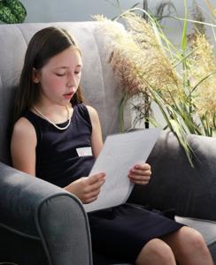 Na zdjęciu znajdują się uczestniczka czytająca książkę siedząc na fotelu. Zdjęcie wykonano w bibliotece.