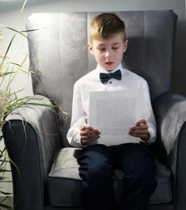 Na zdjęciu znajdują się uczestniczka czytająca książkę siedząc na fotelu. Zdjęcie wykonano w bibliotece.