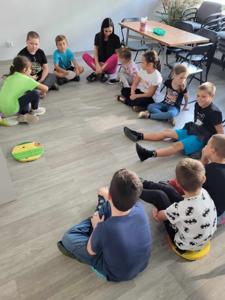 Na zdjęciu znajdują się uczestnicy zajęć. Dzieci siedzą w kręgu.