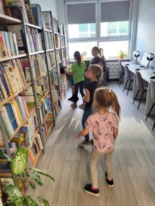 Na zdjęciu znajdują się uczestnicy zajęć. Dzieci znajdują się pomiędzy regałami z książkami.
