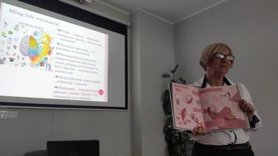 Na zdjęciu znajduje się Prelegent. Zdjęcie wykonano w bibliotece. W tle prezentacja multimedialna.