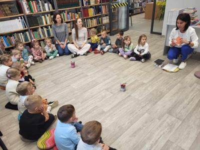 Na zdjęciu znajdują się uczestnicy zajęć. Dzieci wykonują zadania siedząc na poduszkach. Zdjęcie wykonano w bibliotece.