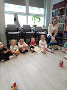 Na zdjęciu znajdują się uczestnicy zajęć. Dzieci wykonują zadania siedząc na poduszkach. Zdjęcie wykonano w bibliotece.