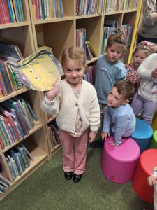 Na zdjęciu znajdują się uczestnicy zajęć. Dzieci wykonują zadania pomiędzy regałami z książkami.  Zdjęcie wykonano w bibliotece.