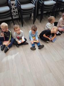 Na zdjęciu znajdują się uczestnicy zajęć. Dzieci wykonują zadania siedząc na poduszkach. Zdjęcie wykonano w bibliotece.