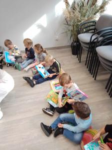 Na zdjęciu znajdują się uczestnicy zajęć. Dzieci wykonują zadania siedząc na poduszkach. Zdjęcie wykonano w bibliotece.