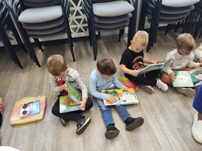 Na zdjęciu znajdują się uczestnicy zajęć. Dzieci wykonują zadania siedząc na poduszkach. Zdjęcie wykonano w bibliotece.
