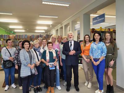 Na zdjęciu znajdują się uczestnicy spotkania autorskiego. Uczestnicy stoją. Zajęcie wykonano w bibliotece.