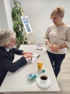 Na zdjęciu znajduje się autor Zbigniew Kołba trzymający książkę. W tle uczestnicy spotkania.