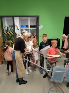 Na zdjęciu znajdują się uczestnicy warsztatów. Dzieci stoją i wieszają prace na suszarce. Zdjęcie wykonano w bibliotece.