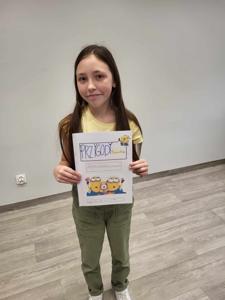 Na zdjęciu znajduje się uczestniczka warsztatów. Dziewczyna trzyma w ręce komiks. Zdjęcie wykonano w bibliotece.