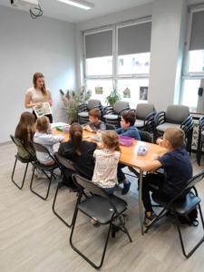 Na zdjęciu znajdują się uczestnicy warsztatów. Młodzież siedzi przy stole, wykonuje oraz ogląda komiksy. Zdjęcie wykonano w bibliotece.
