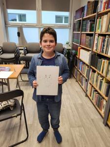 Na zdjęciu znajduje się uczestnik warsztatów. Chłopak trzyma komiks. Zdjęcie wykonano w bibliotece.