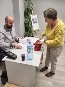 Na zdjęciu znajduje się prelegent siedzący przy biurku. Jedna osoba stoi przy biurku.