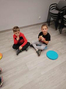 Na zdjęciu znajdują się uczestnicy warsztatów. Dzieci siedzą na podłodze.