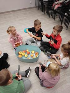 Na zdjęciu znajdują się uczestnicy warsztatów. Dzieci siedzą w kręgu - w środku jabłka w misce.