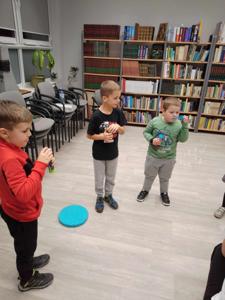 Na zdjęciu znajdują się uczestnicy warsztatów. Dzieci stoją i dmuchają  bański.