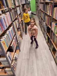 Na zdjęciu znajdują się uczestnicy warsztatów. Dzieci stoją. W tle księgozbiór biblioteki.