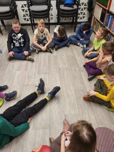 Na zdjęciu znajdują się uczestnicy zajęć. Dzieci siedzą na podłodze.