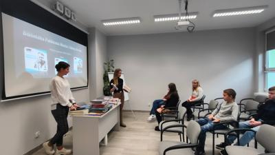 Na zdjęciu znajdują się uczestnicy wykładu. Młodzież siedzi na krzesłach. Prelegentki wyświetlają prezentacje multimedialną.