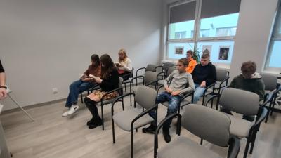 Na zdjęciu znajdują się uczestnicy wykładu. Młodzież siedzi na krzesłach. Młodzież trzyma w rękach książki.
