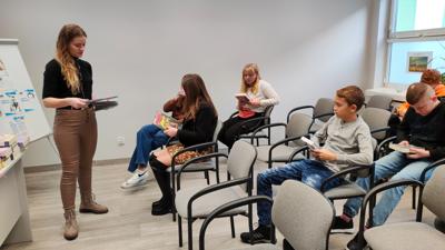 Na zdjęciu znajdują się uczestnicy wykładu. Młodzież siedzi na krzesłach. Prelegentki wyświetlają prezentacje multimedialną.