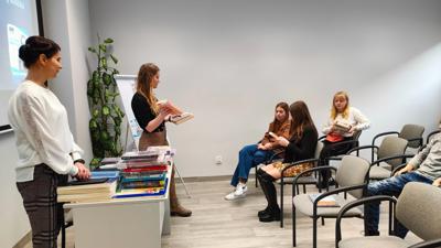 Na zdjęciu znajdują się uczestnicy wykładu. Młodzież siedzi na krzesłach. Prelegentki wyświetlają prezentacje multimedialną.