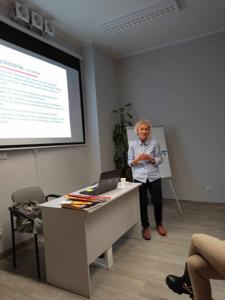 Na zdjęciu znajduje się prelegentka. W tle prezentacja multimedialna. Zdjęcie wykonano w bibliotece.