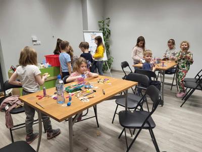 Na zdjęciu znajdują się uczestnicy warsztatów. Dzieci siedzą przy stole i wykonują prace plastyczne. Zdjęcie wykonano w bibliotece.